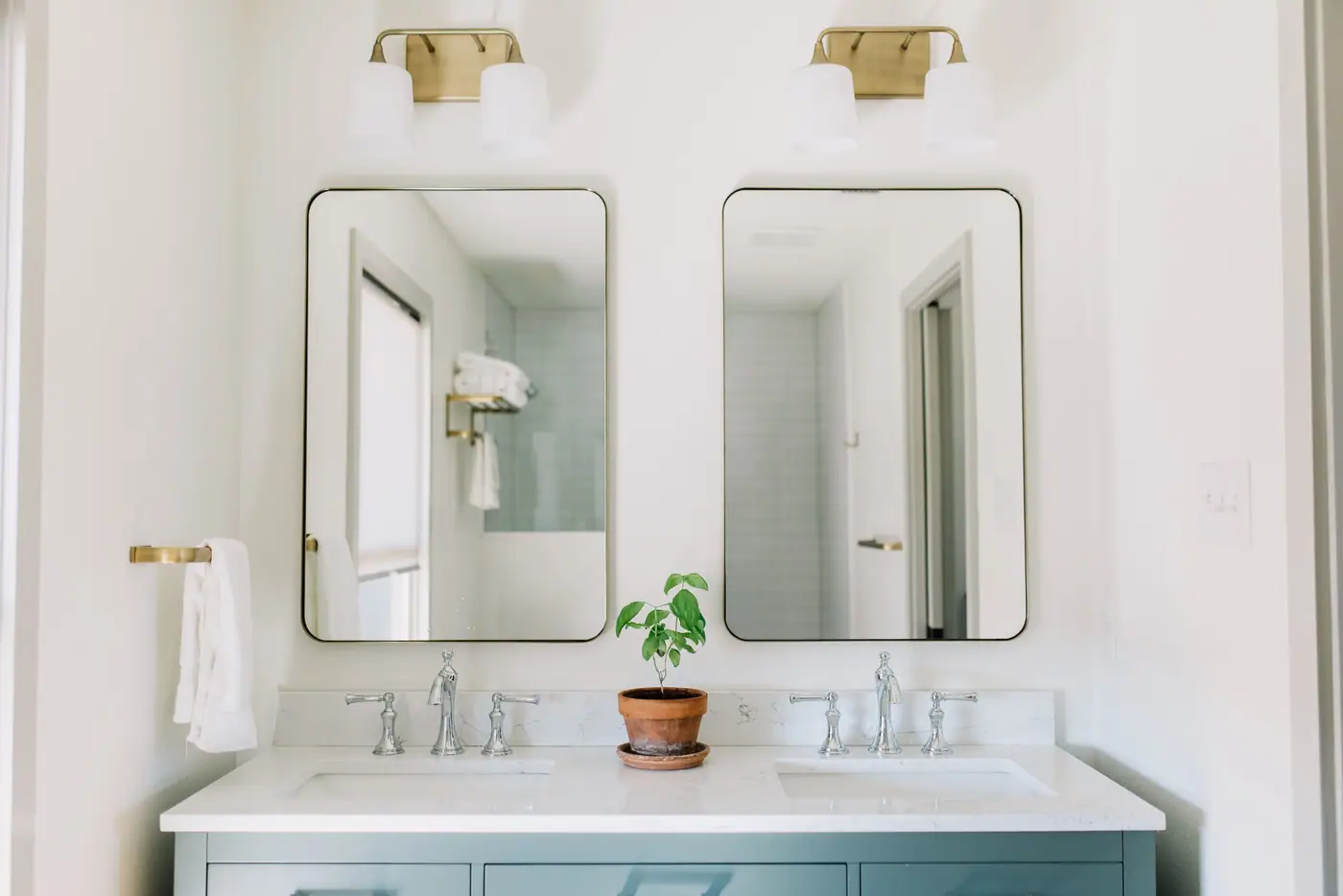 A blue-gray double vanity under two brass sconces and thin black-framed mirrors in an Aledo bath