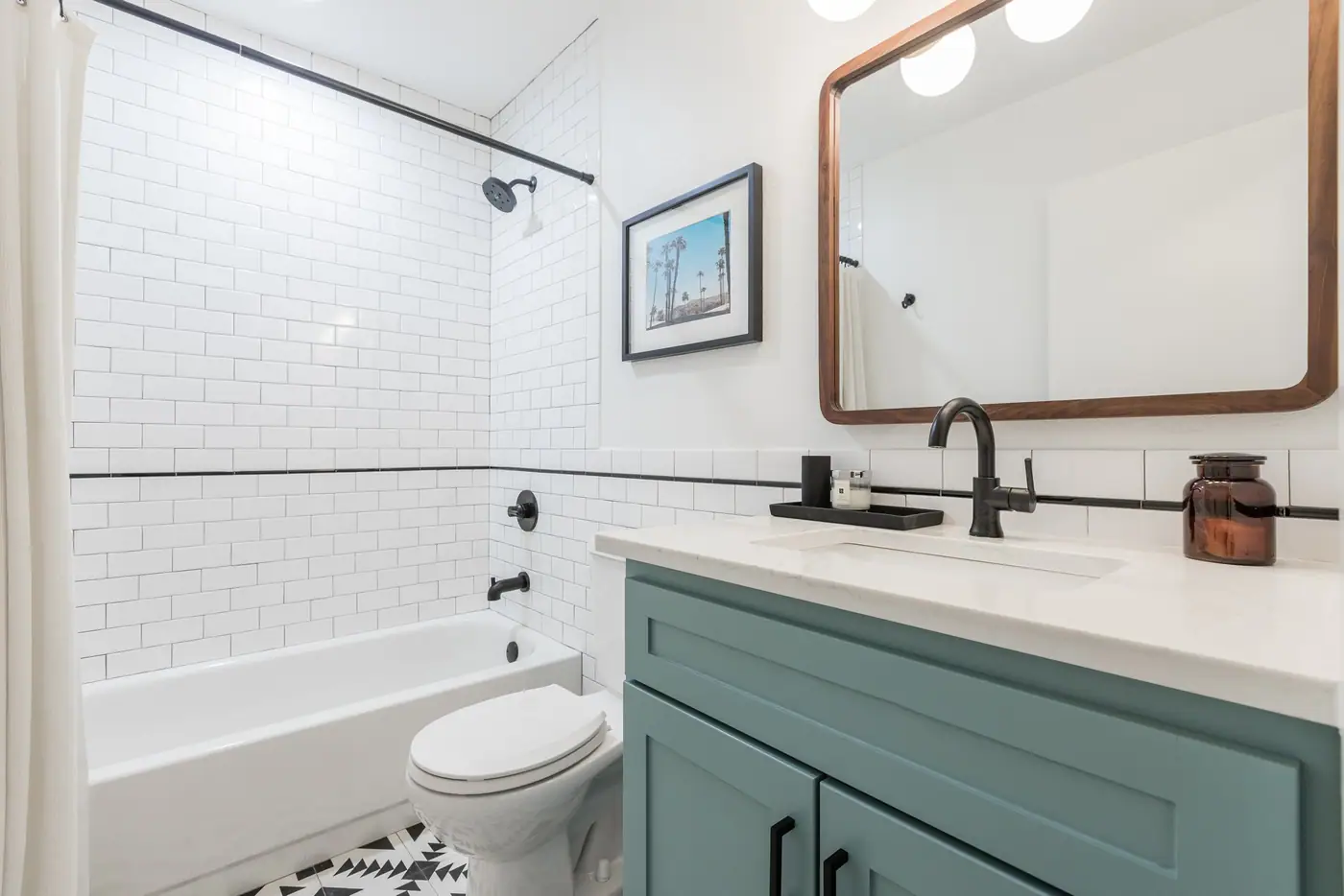 A teal vanity with black fixtures, a wood-framed mirror, and a white subway tub and shower in an Arlington Heights hall bath