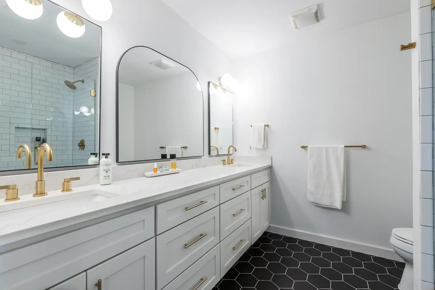 A white double vanity with brass fixtures and a black hex floor in an Arlington Heights primary suite