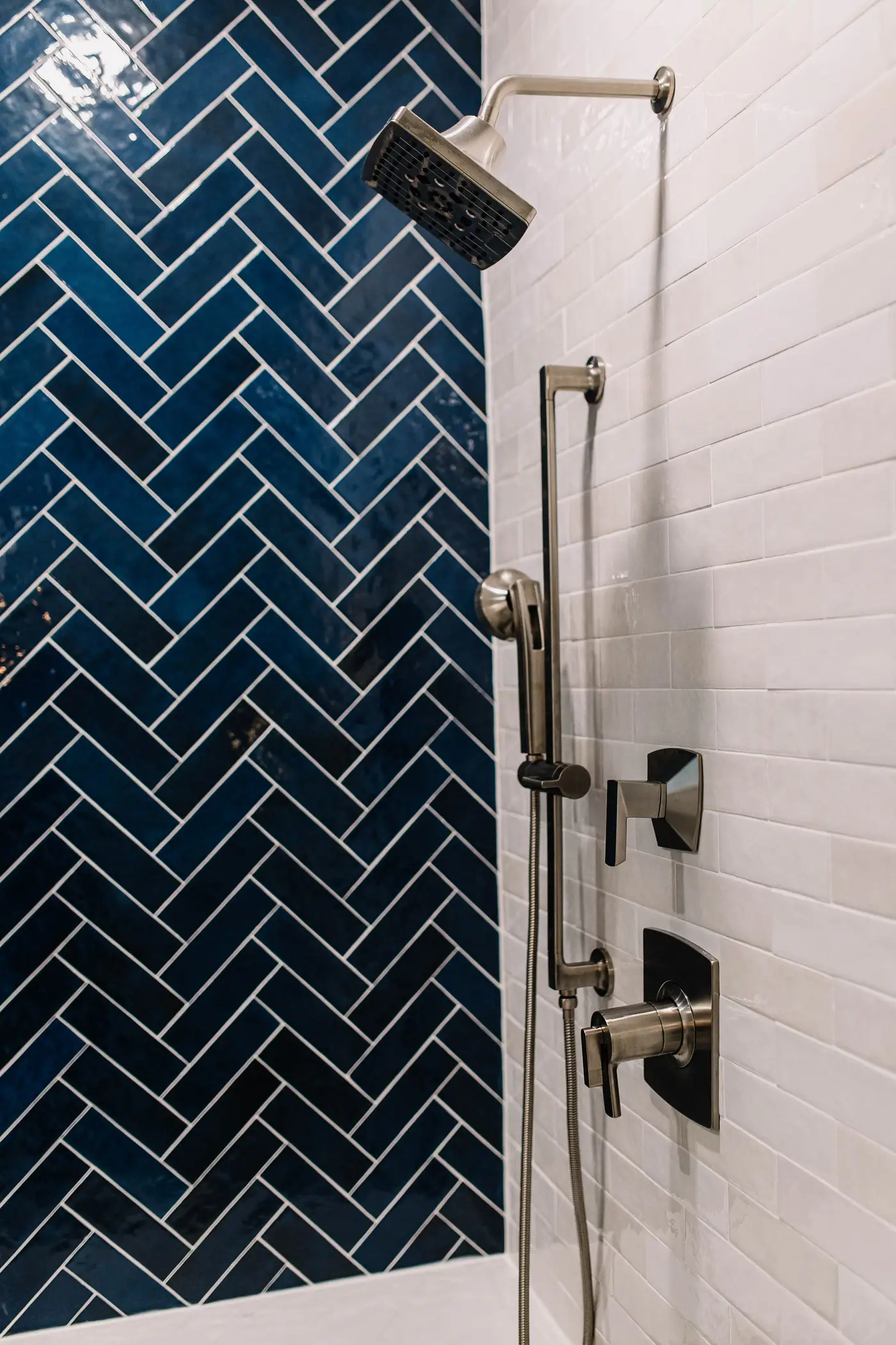 Navy herringbone tile beside a white subway wall with a nickel-toned shower head, hand shower, and valves in a Mansfield primary suite remodel