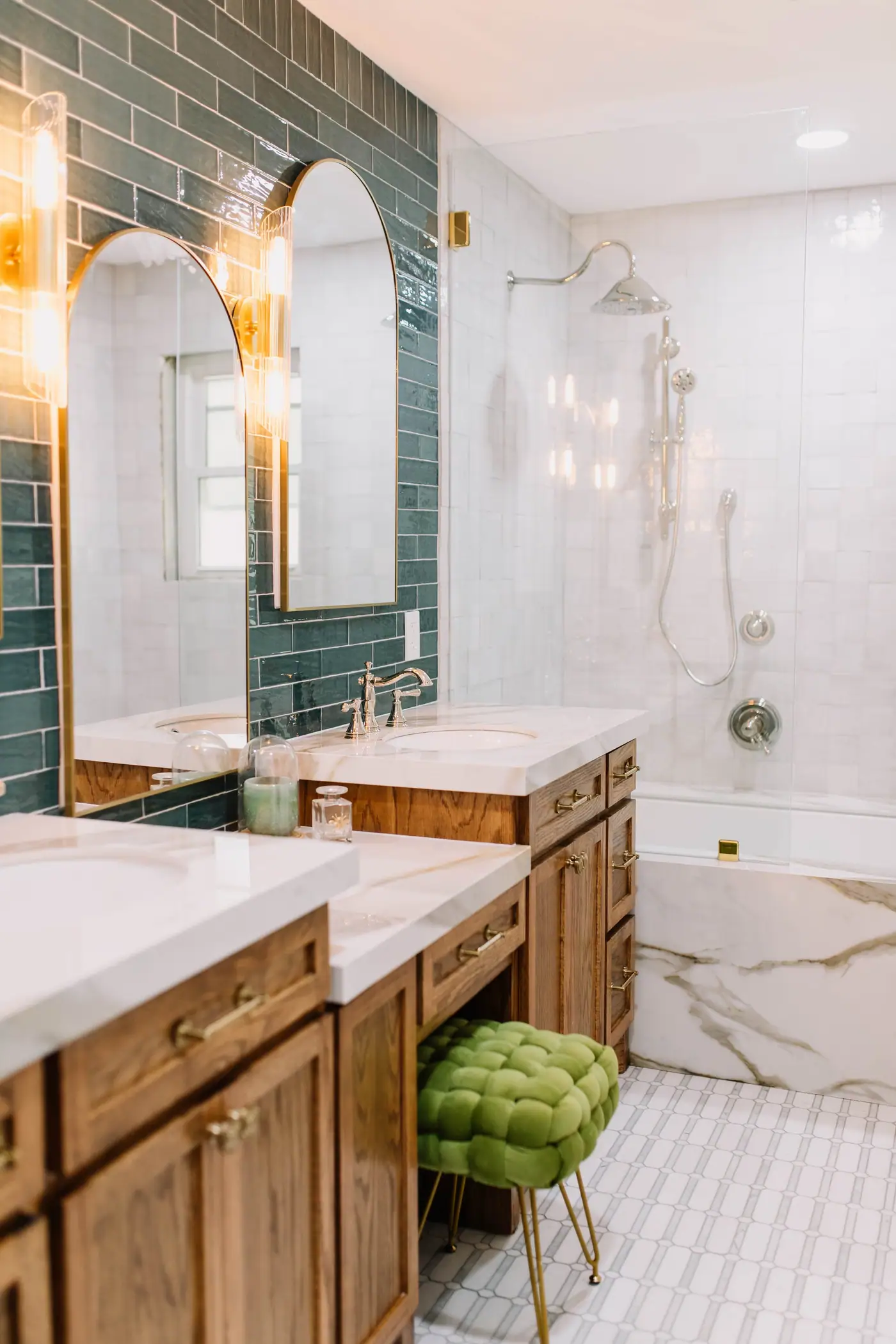 Twin arched brass mirrors over a wood vanity beside a glass shower in the Wedgwood primary suite