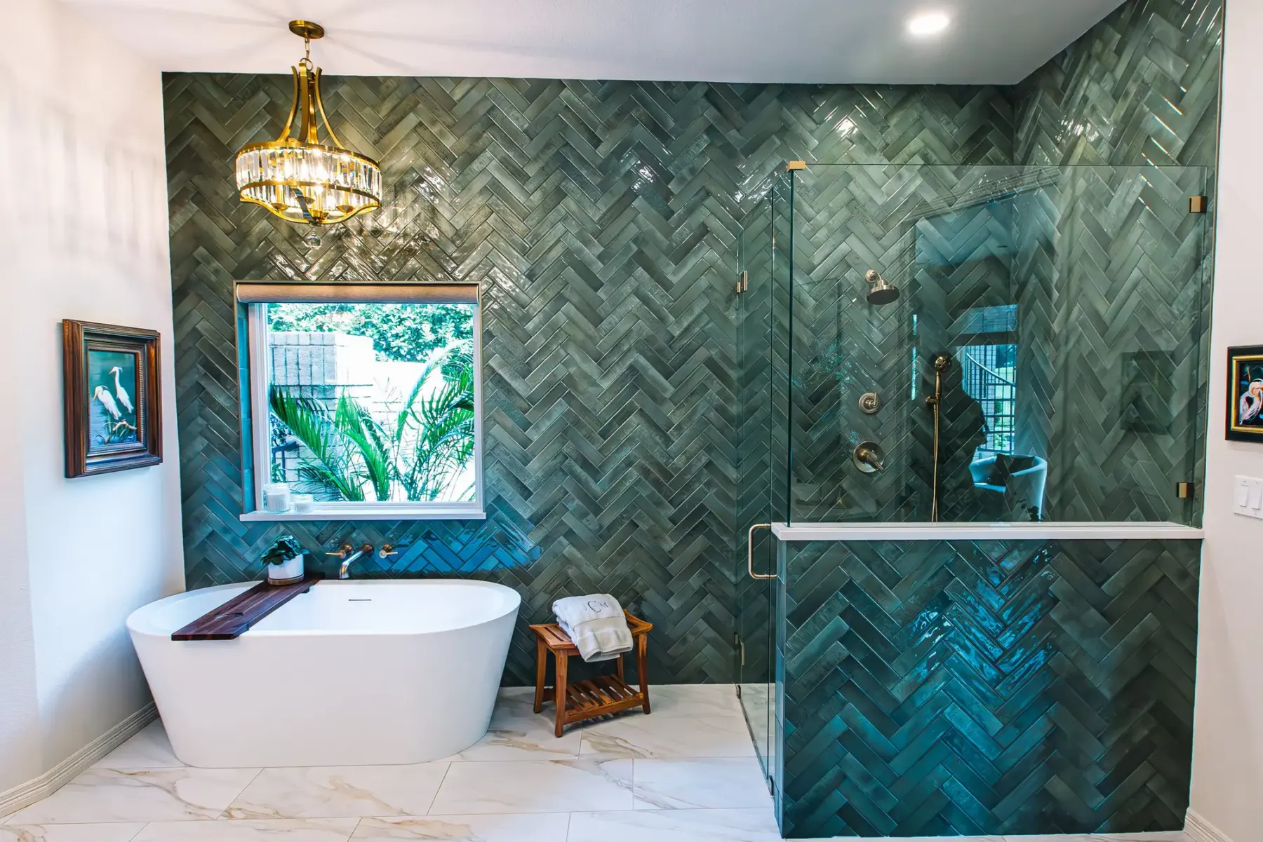 A Fort Worth primary bath remodel with a freestanding tub under a window, an emerald herringbone tile wall, a brass chandelier, and a frameless glass shower